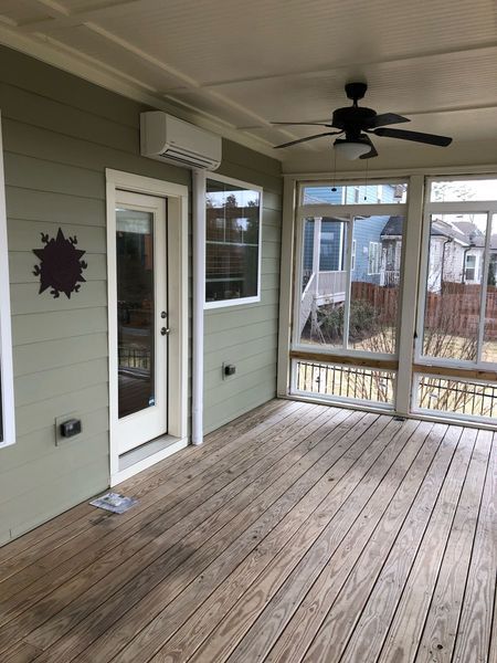 Sunroom with wood floors, pale green walls, a white door, and an air conditioning unit.