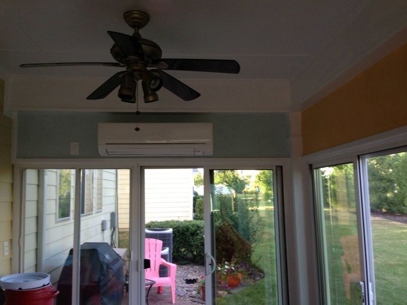 Sunroom with sliding glass doors, air conditioning unit, ceiling fan, and view of a yard.
