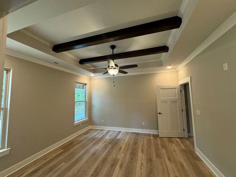 Bedroom with wood beams, light brown walls, wooden floor, white trim, and a ceiling fan.