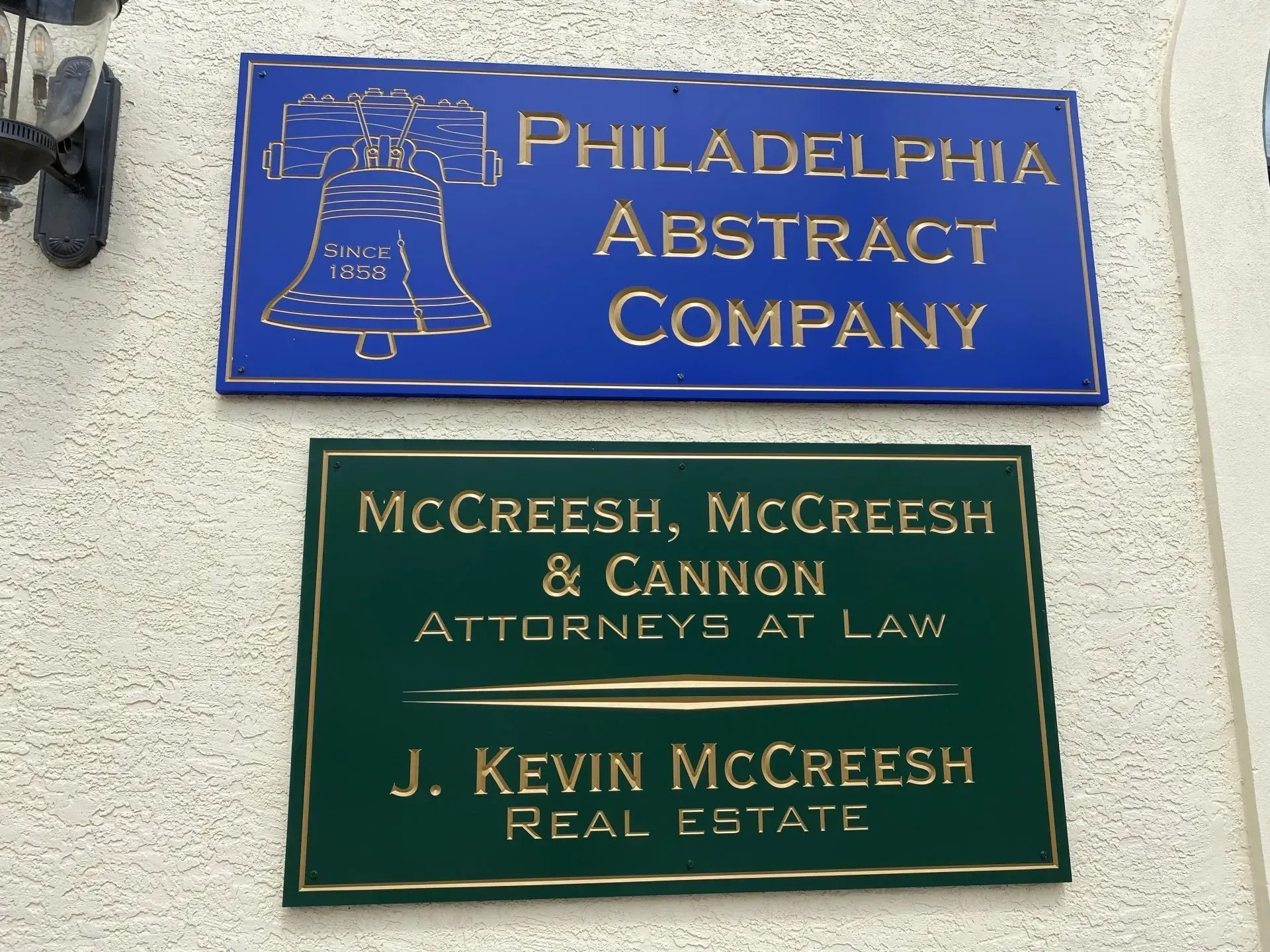 Two signs on a textured wall: Philadelphia Abstract Company (blue) and McCreesh, McCreesh & Cannon, Attorneys at Law, J. Kevin McCreesh, Real Estate (green).