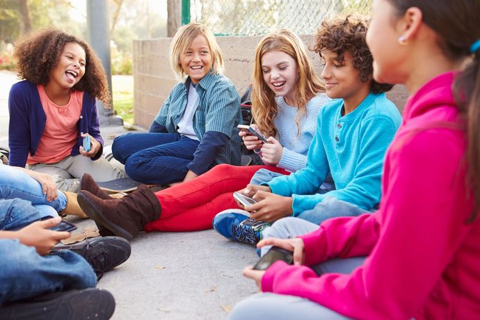 A group of children are sitting in a circle on the ground looking at their phones.