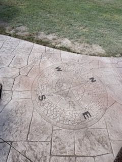 Stamped concrete patio with compass rose design, bordered by green grass.