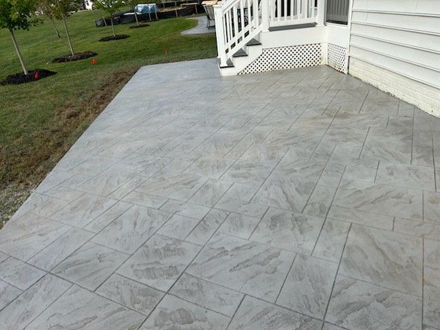 Gray stamped concrete patio next to a house with white stairs, leading to a grassy lawn.