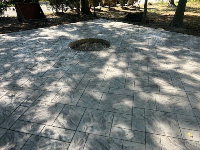 Stamped concrete patio with a circular fire pit, shaded by trees.