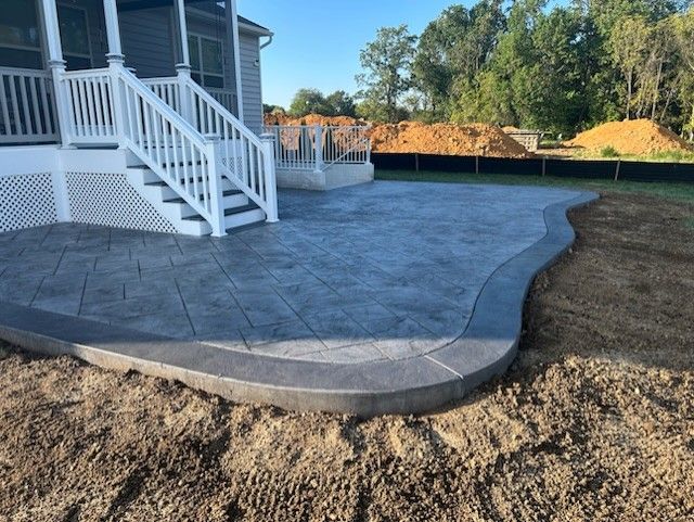 Concrete patio with textured surface and curved edge next to a deck with white stairs.