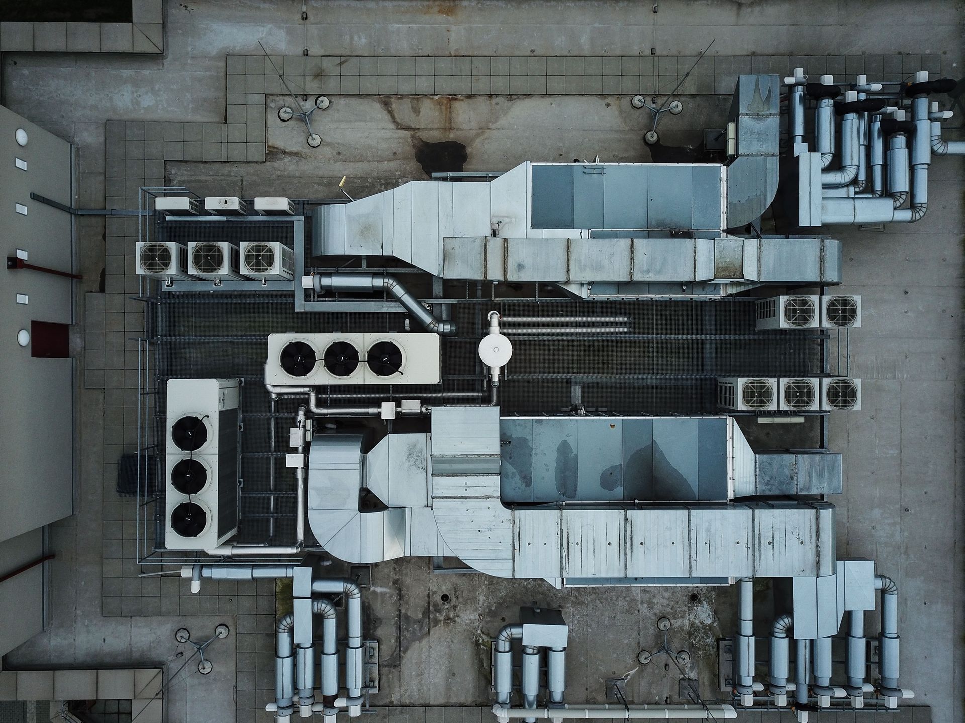 An aerial view of industrial HVAC rooftop units, metal ductwork, and cooling fans arranged on a building rooftop.