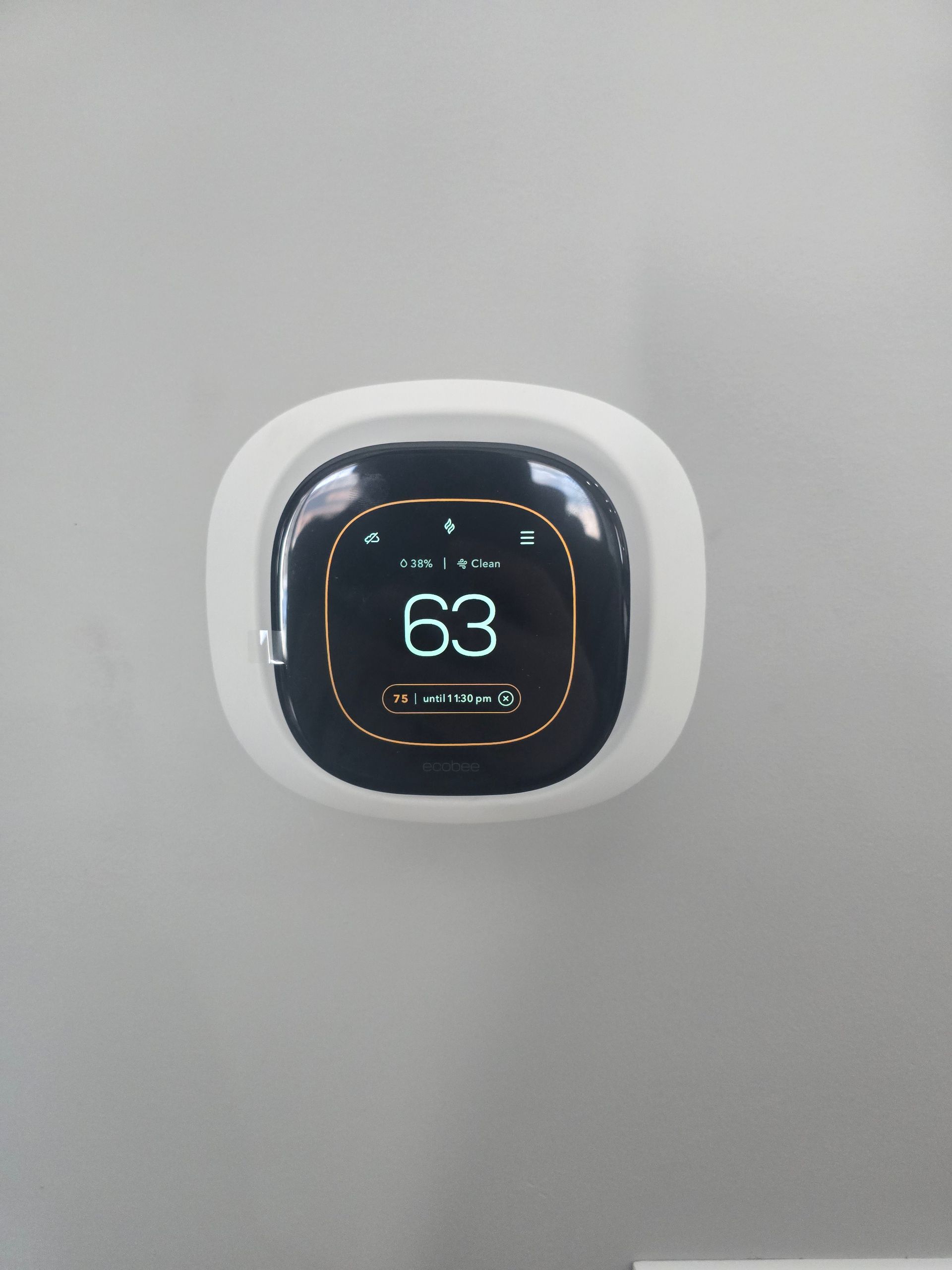 A white, square smart thermostat on a grey wall displaying the number 63 on a black digital screen.