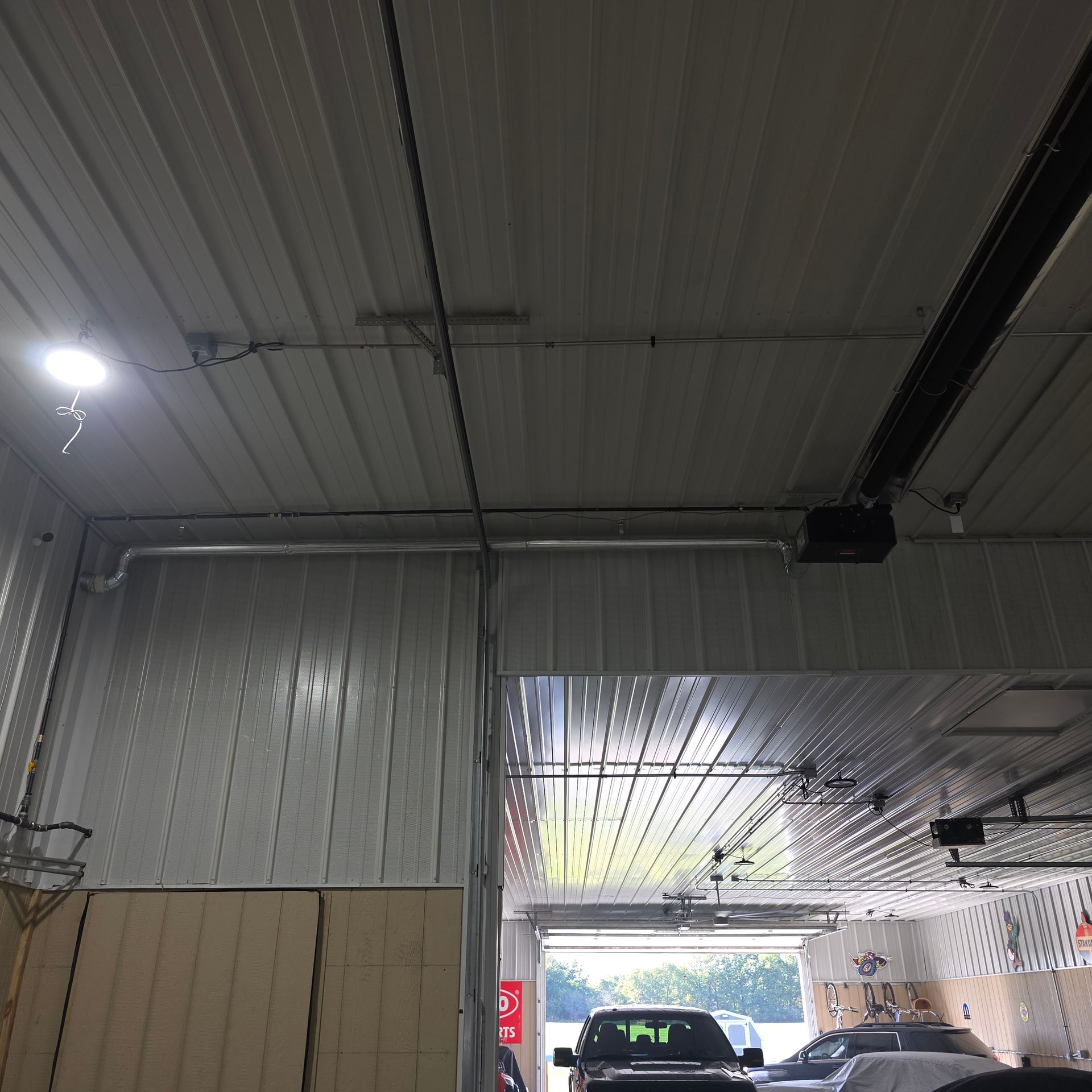 Interior view of a garage with a metal ceiling, bright LED light, and a vehicle visible through the open doorway.