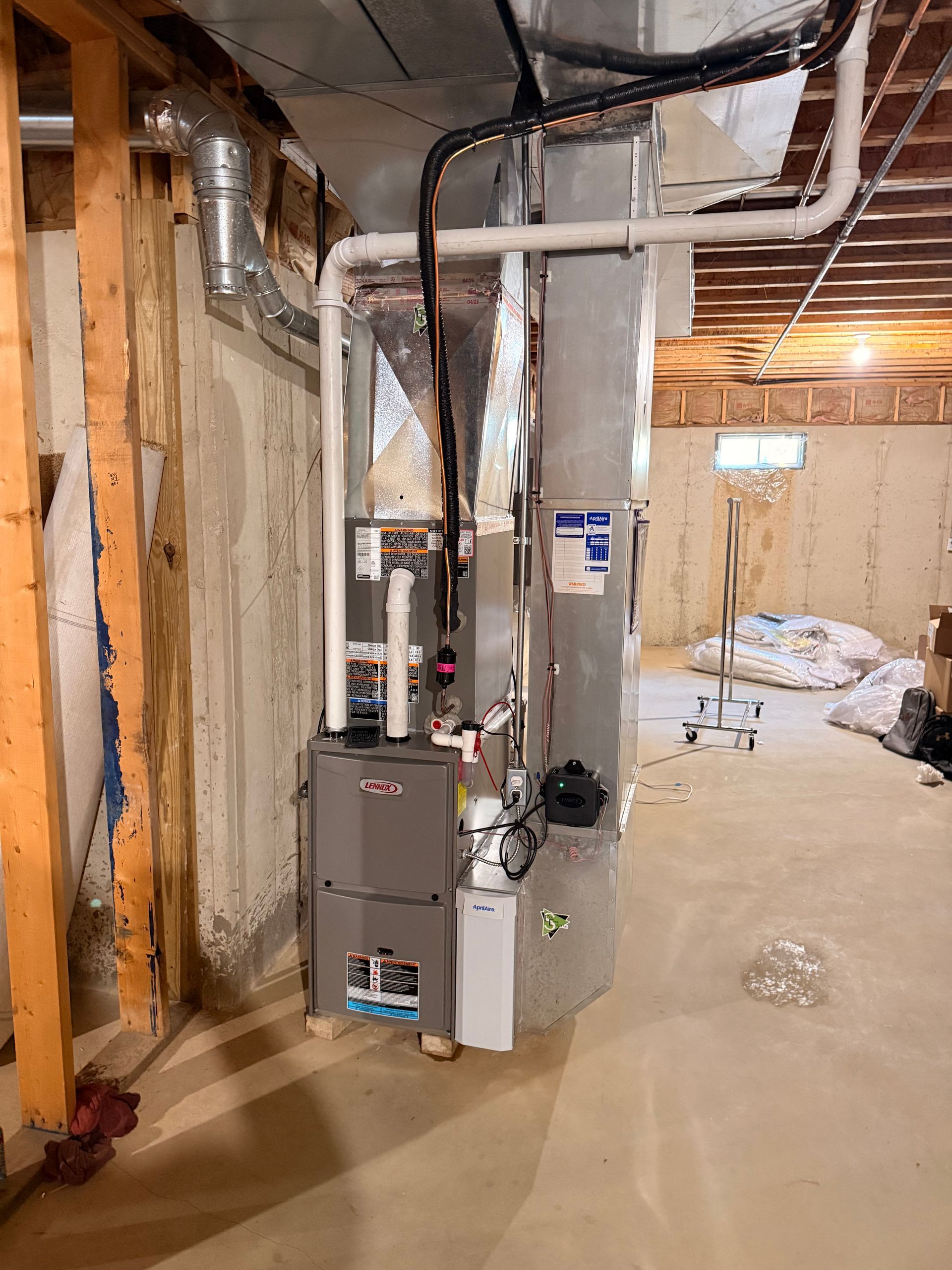 A high-efficiency gas furnace and silver ductwork installed in an unfinished basement with concrete walls.