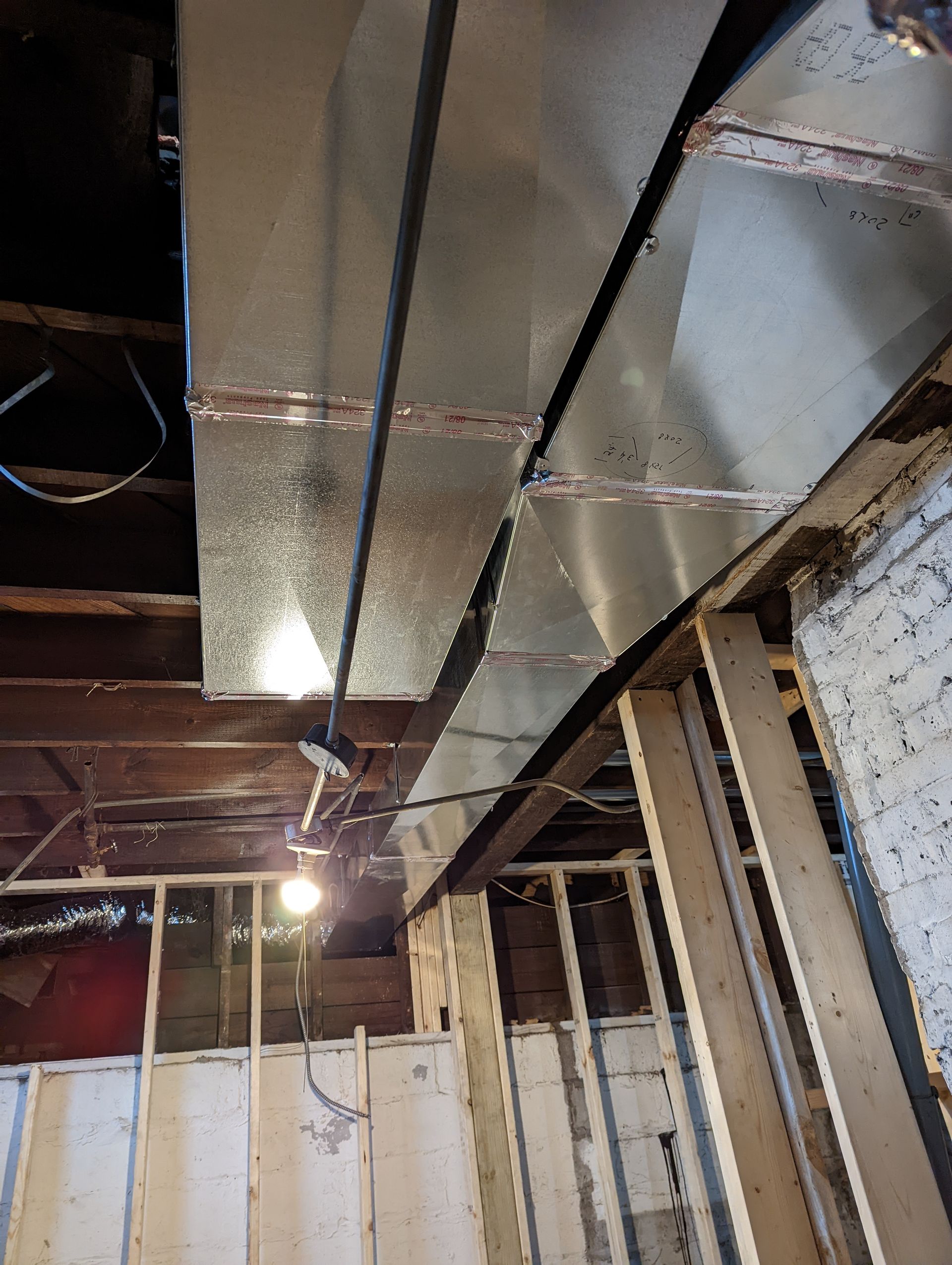 New metal ductwork installed in an unfinished basement with wooden wall framing and exposed structural beams.