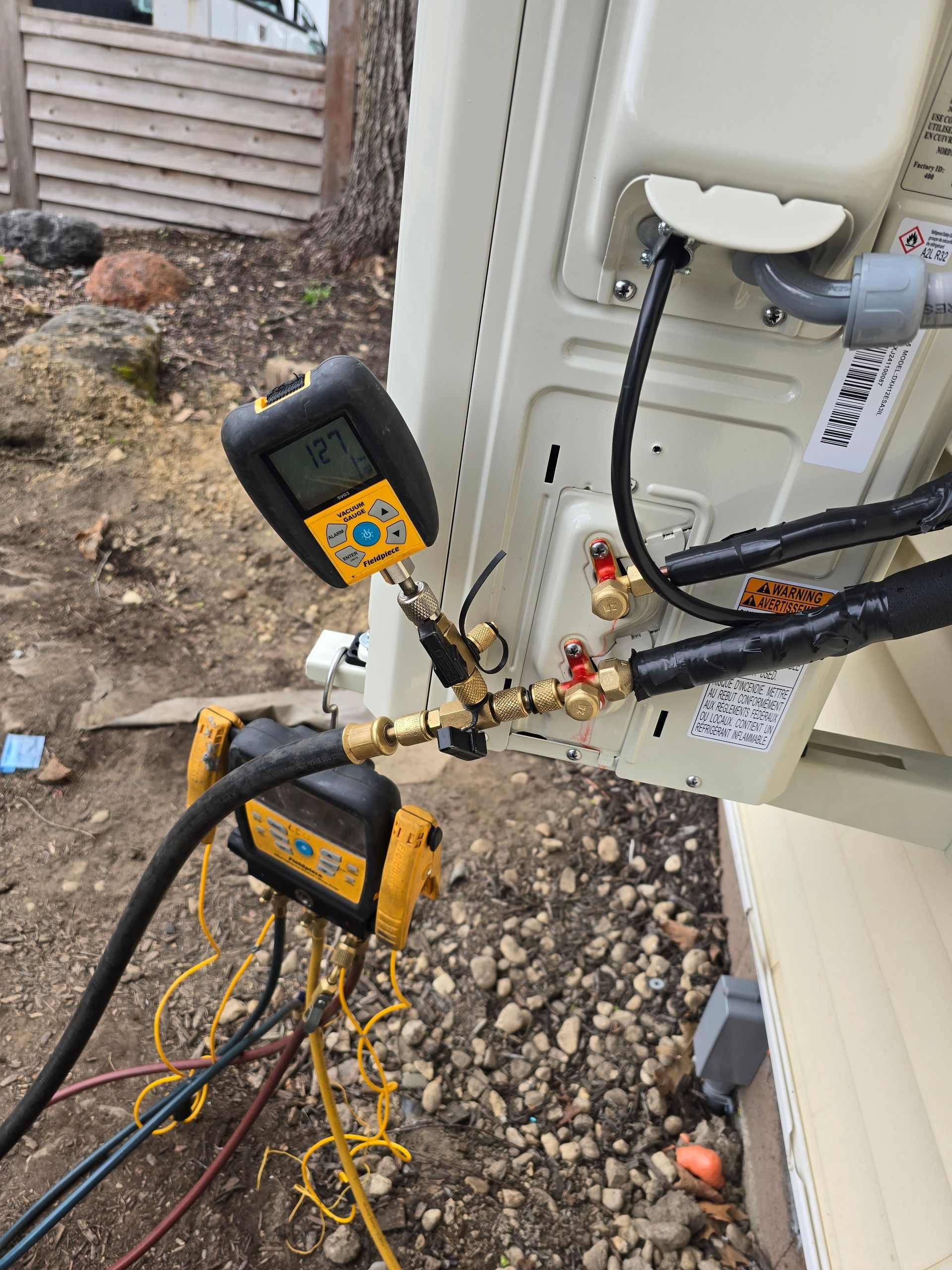 Digital manifold gauges connected to the service ports of an outdoor HVAC unit to monitor refrigerant pressure levels.