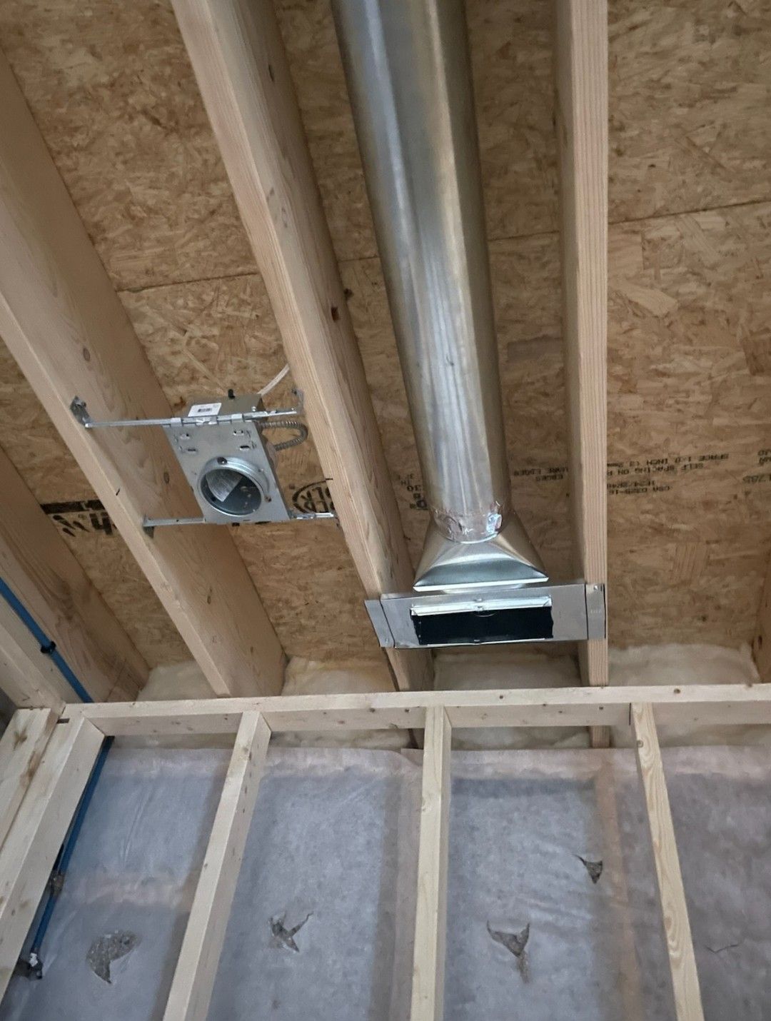 Exposed wooden floor joists in an unfinished ceiling featuring a metal HVAC duct and an electrical junction box.