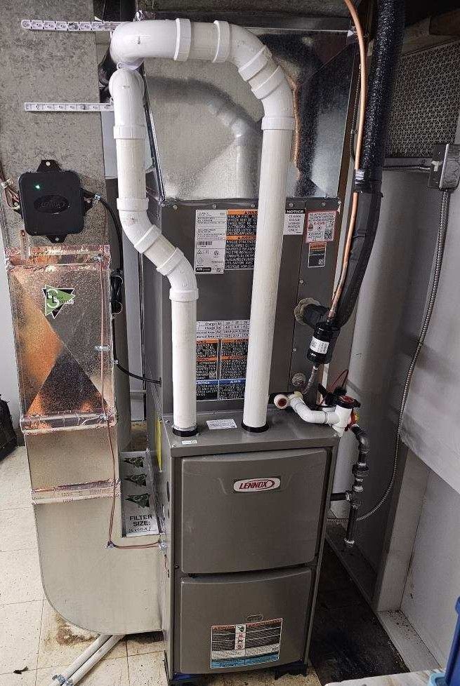 A gray Lennox HVAC furnace unit with white PVC intake and exhaust pipes installed in a basement mechanical area.