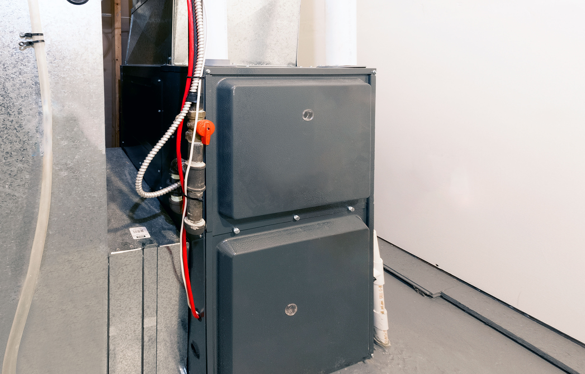 Three grey outdoor HVAC condenser units sitting on concrete pads against a light-colored exterior wall.