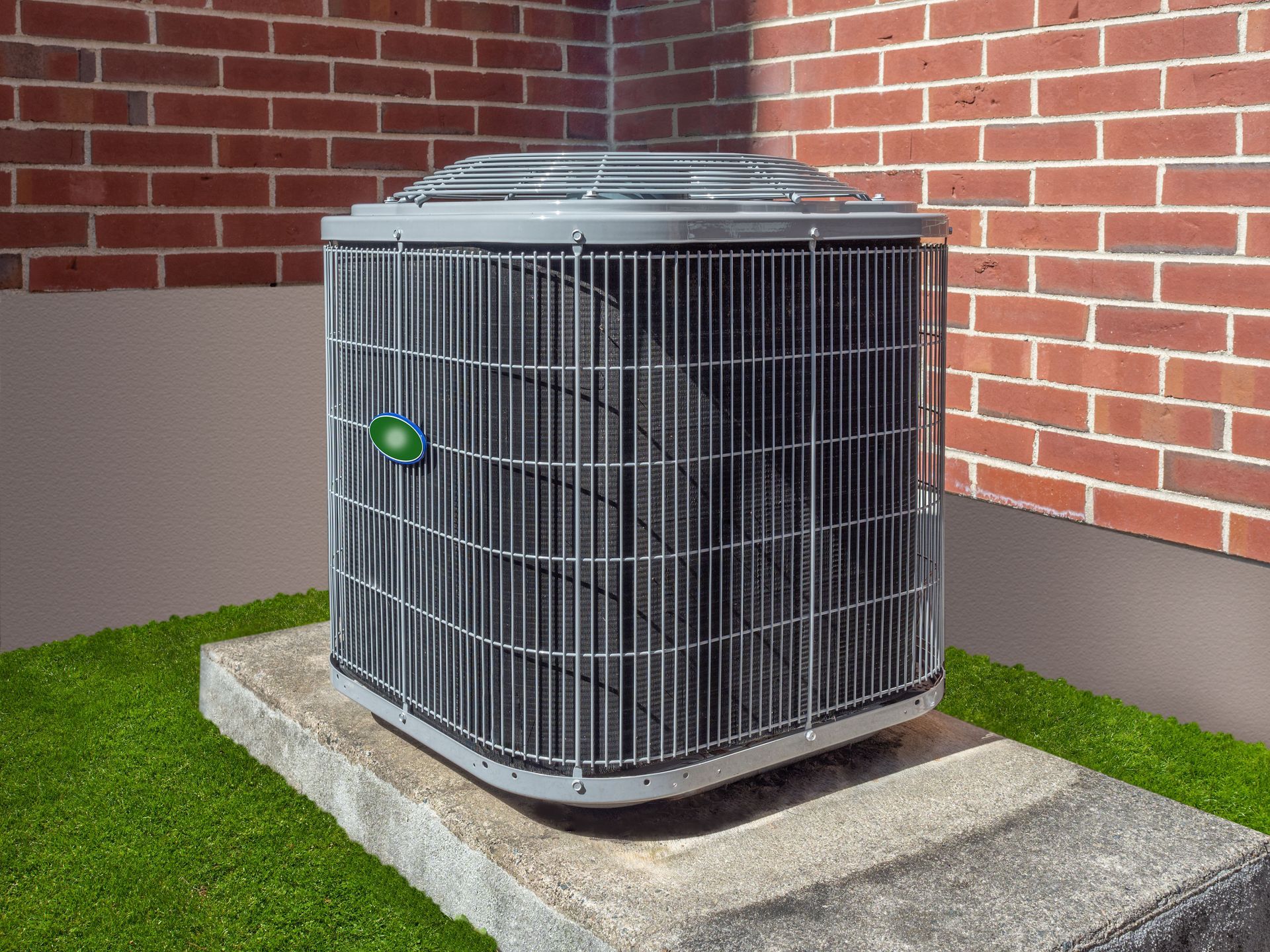 An outdoor gray central air conditioning unit sits on a concrete pad against a red brick wall.