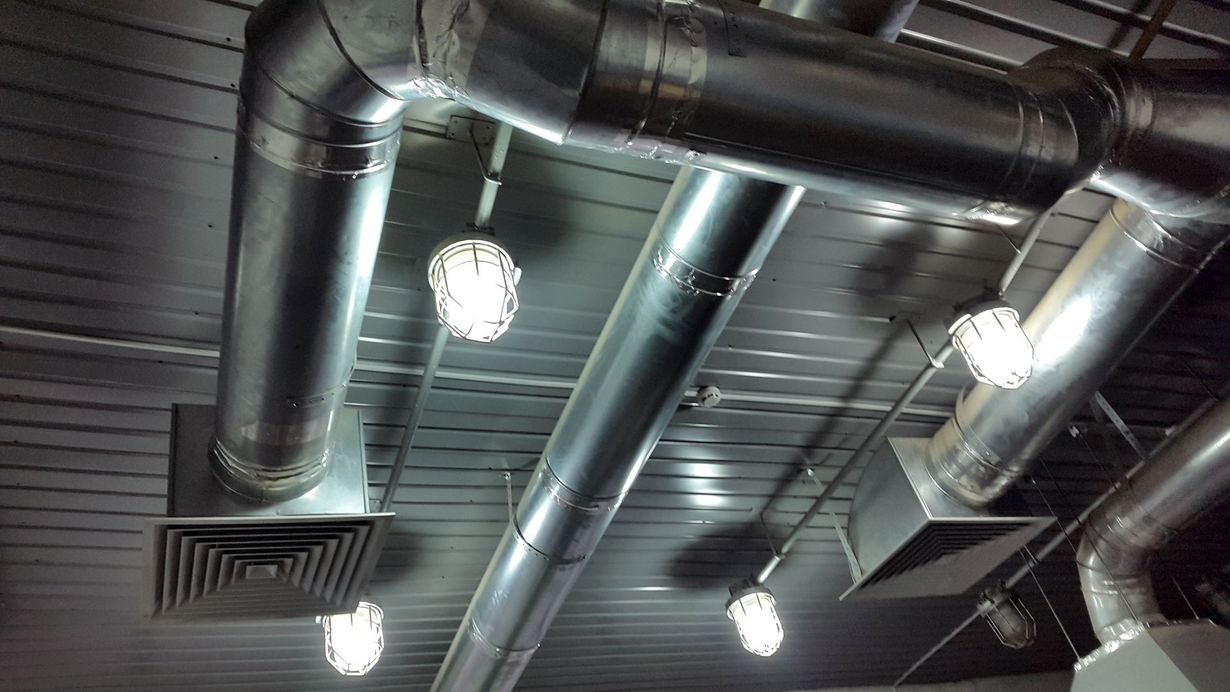 A ceiling view showing exposed metal air ducts, square ventilation registers, and several hanging industrial-style lamps.