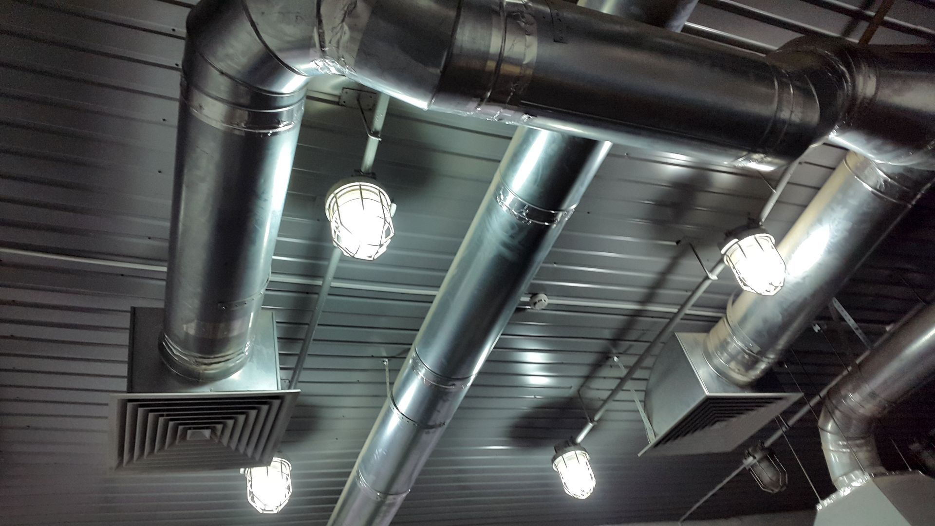 A ceiling view showing exposed metal air ducts, square ventilation registers, and several hanging industrial-style lamps.