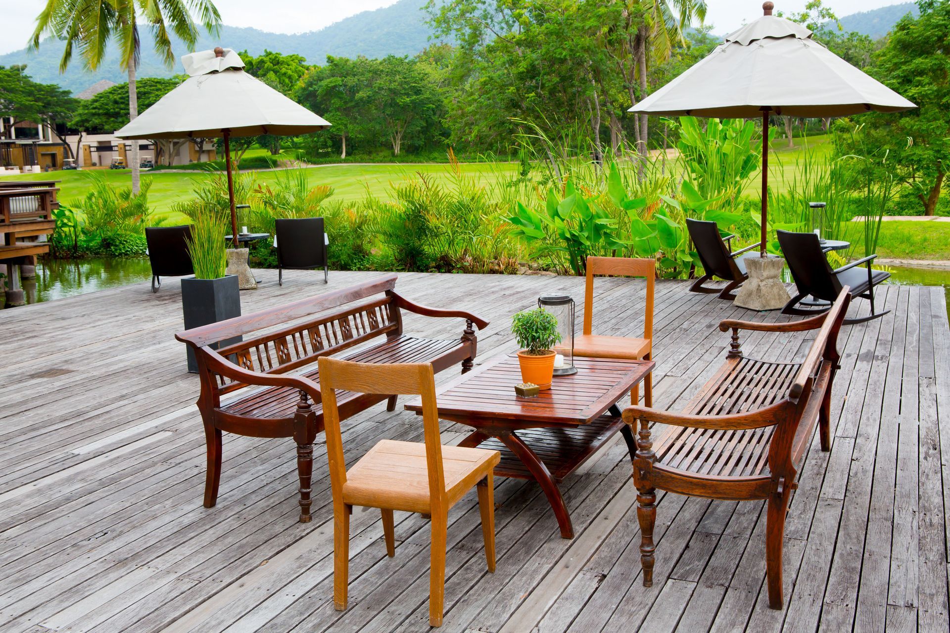 Wooden deck with two benches, a small table, and chairs under umbrellas, overlooking a grassy field and hills.