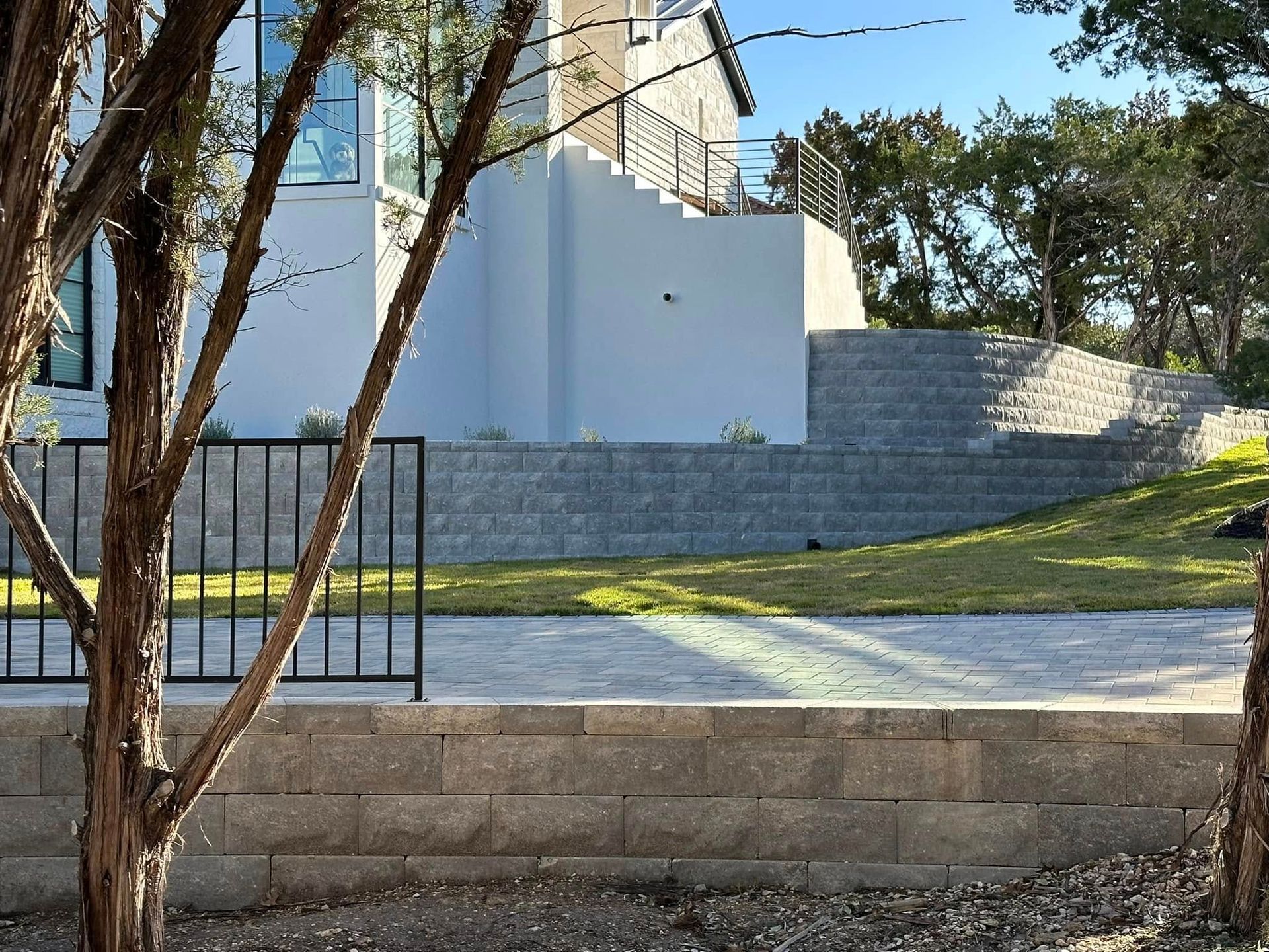 Stone steps and ramp beside a white building, with trees and a metal fence in front.