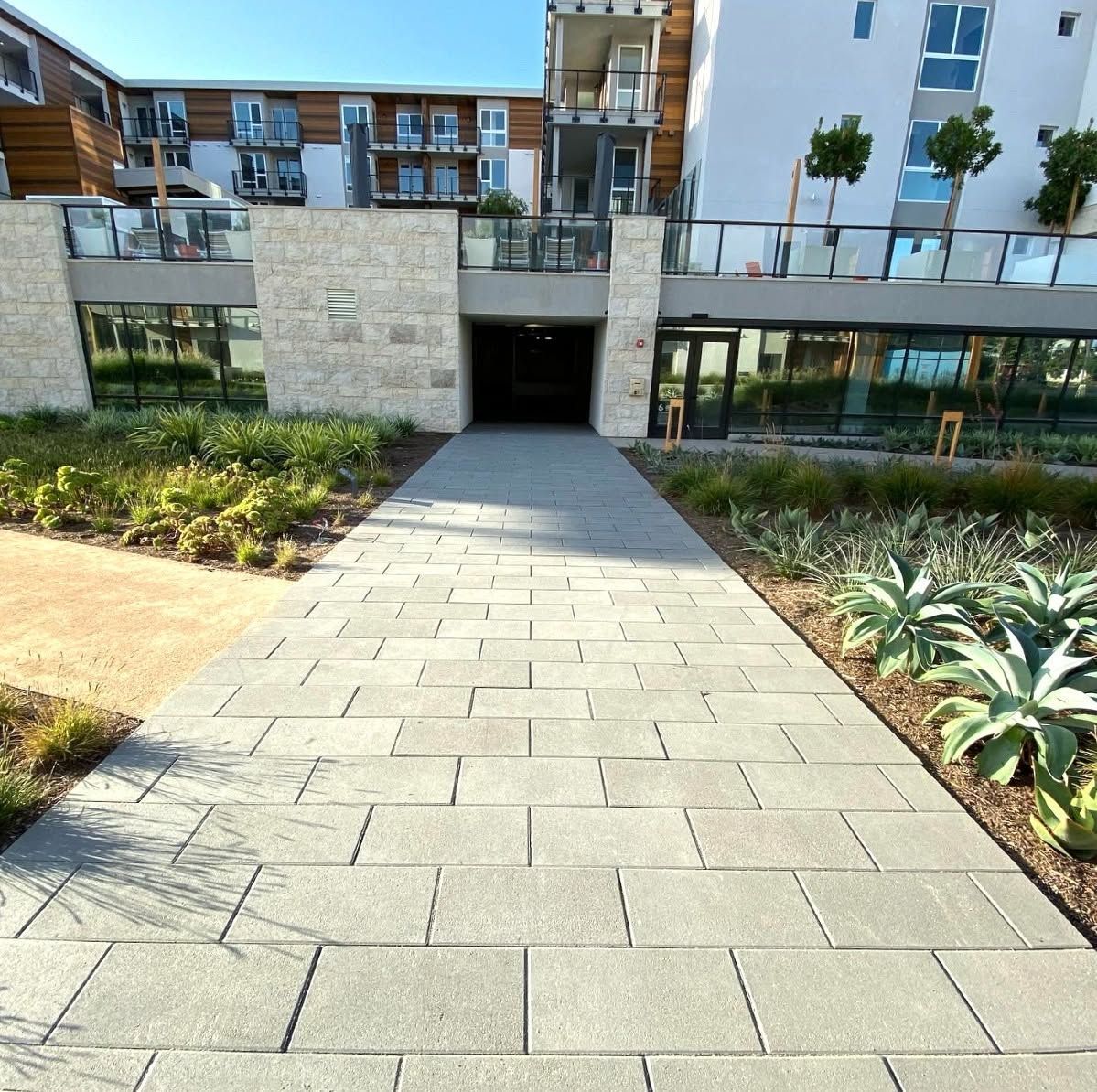 Stone walkway leading to a modern apartment entrance with landscaped beds on both sides