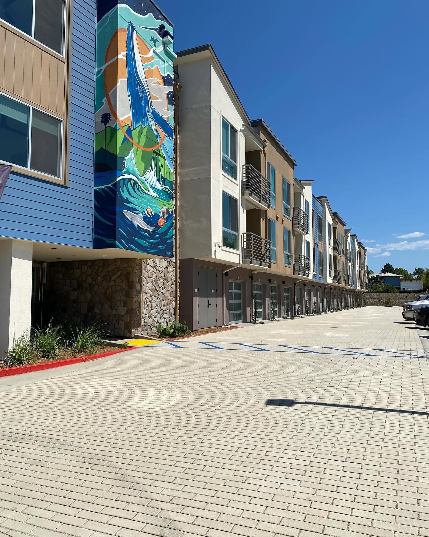 Modern apartment building with colorful mural and paved courtyard under a clear blue sky