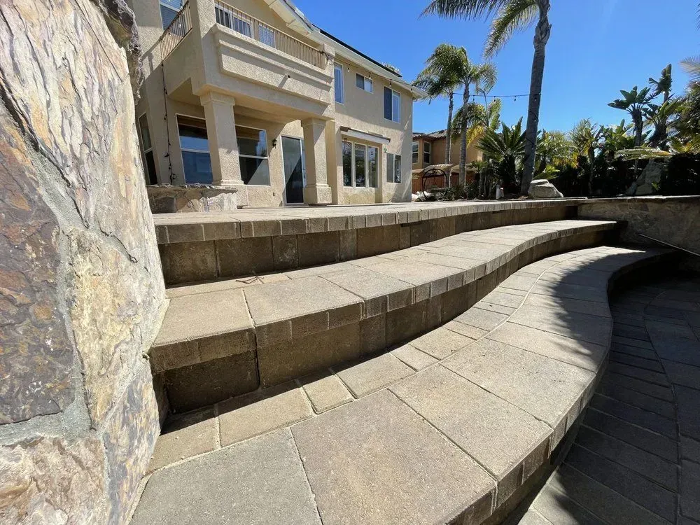 Curved stone steps and terrace beside a luxury house with palm trees in bright sunlight.