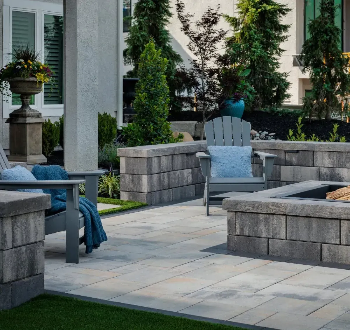 Patio seating area with gray stone benches, blue cushions, and lush greenery around a paved courtyard.