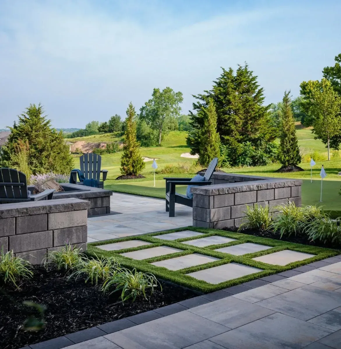 Modern patio with stone seating, stepping stones, and green lawn under a clear blue sky.