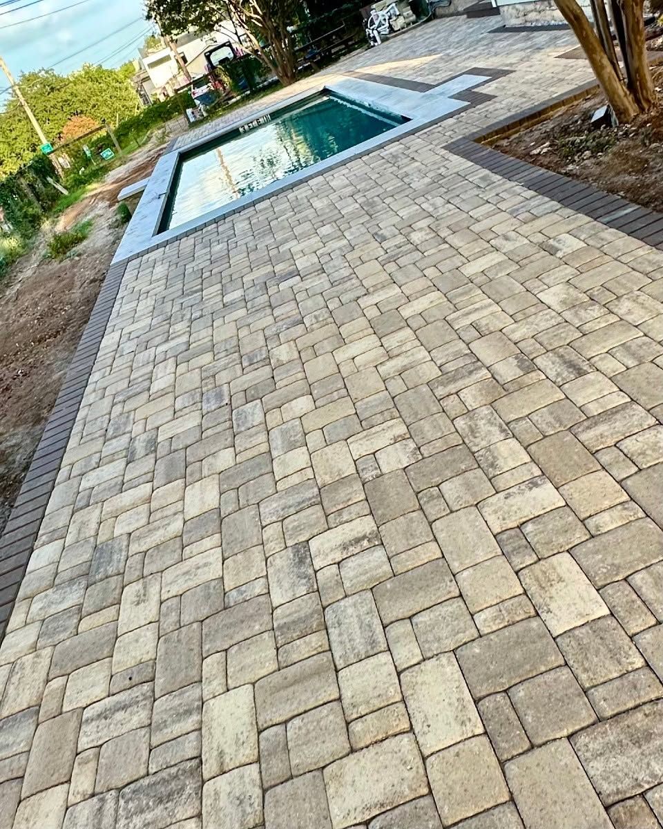 Stone-paver patio beside a rectangular swimming pool in a landscaped yard