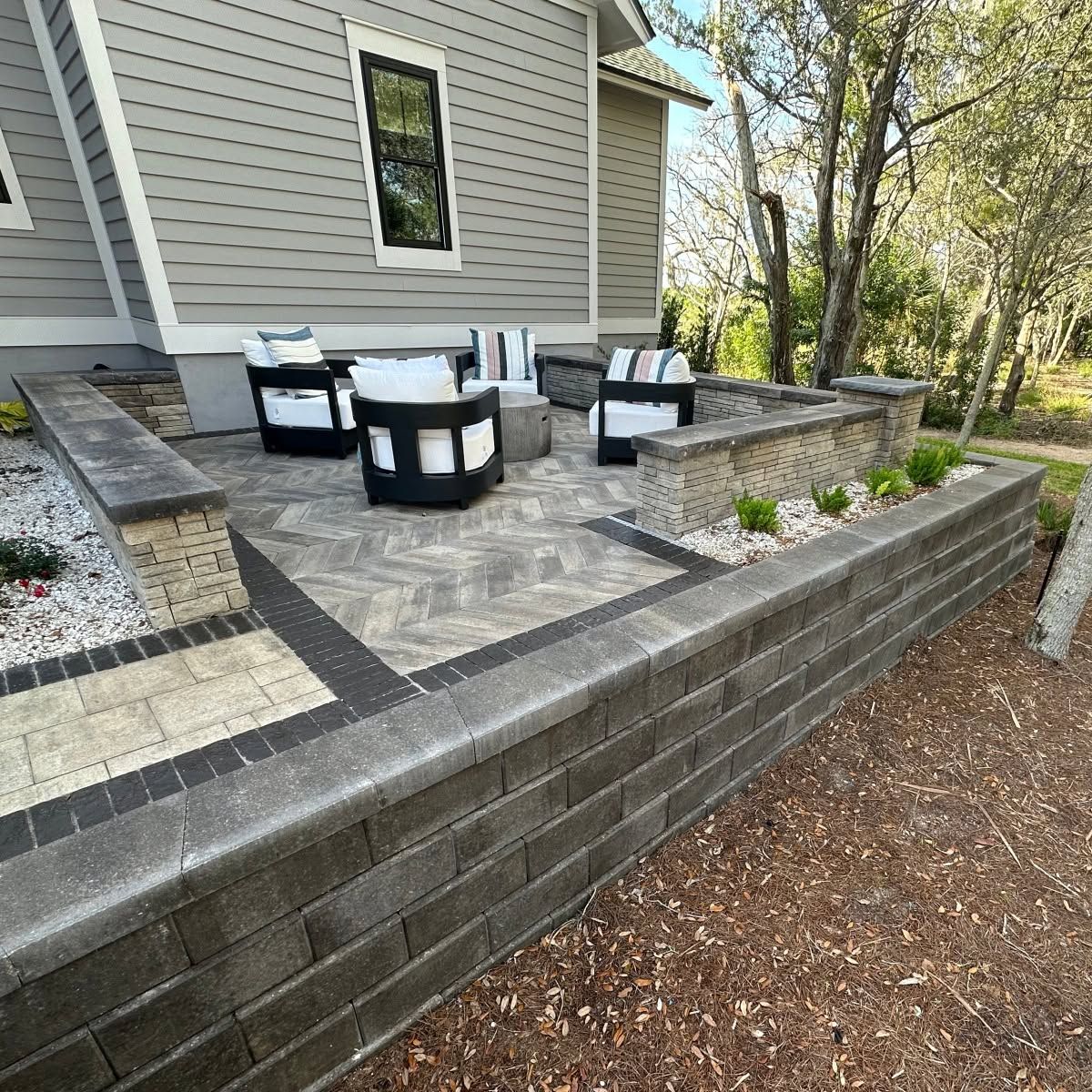 Patio with black-and-white outdoor seating on a raised stone terrace beside a house.