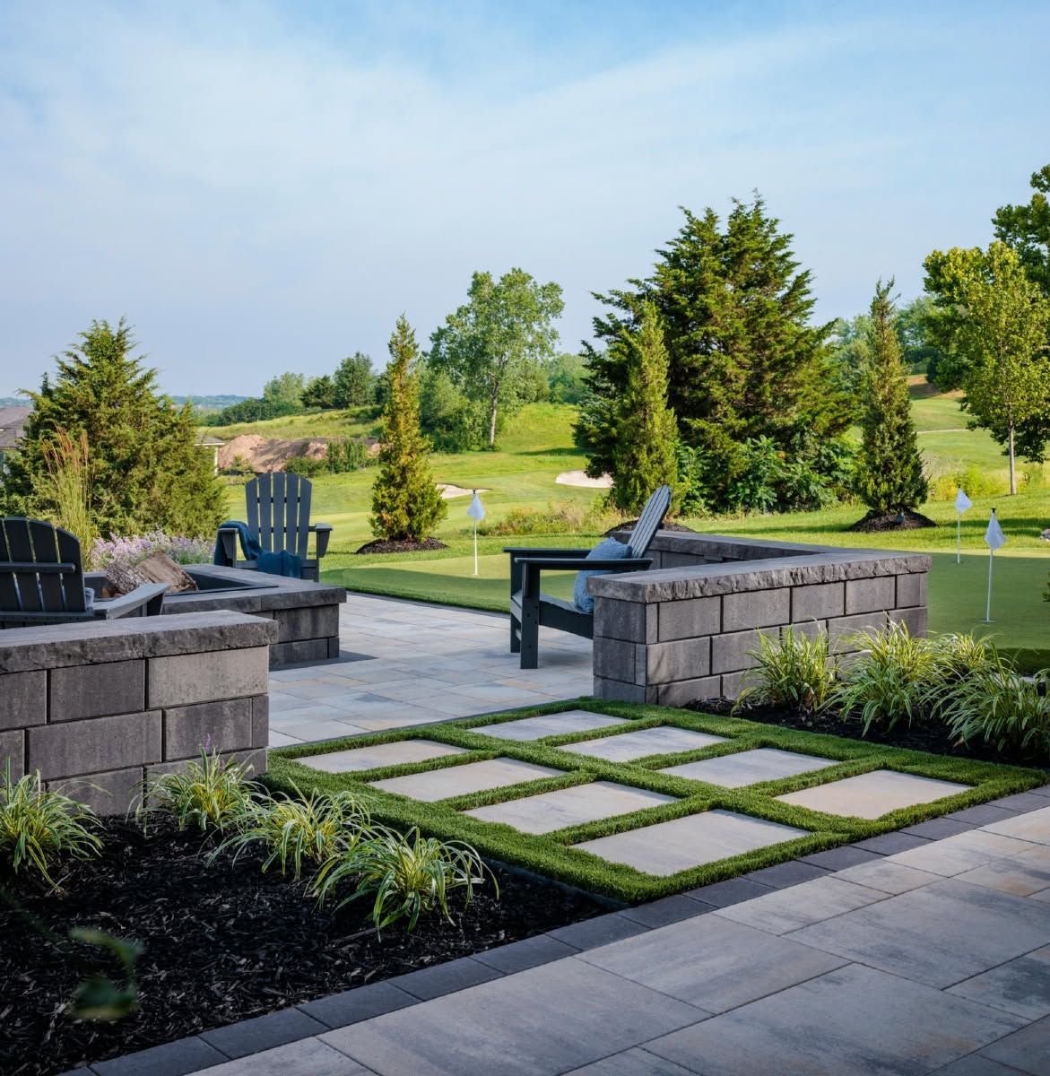 Patio with stone seating, pavers, and Adirondack chairs overlooking a landscaped green garden