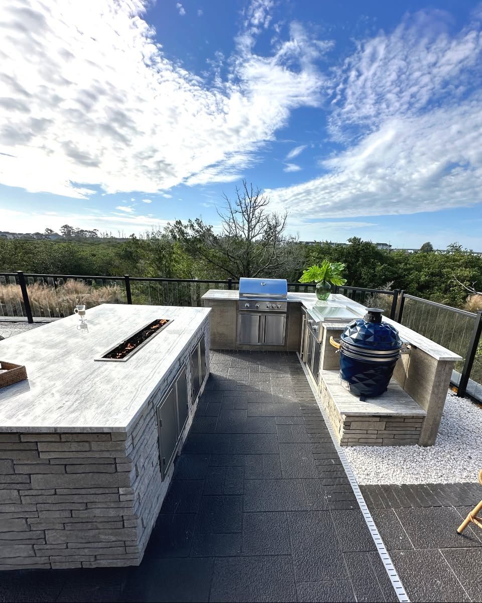 Outdoor patio with built-in grill, stone counters, and a blue ceramic water cooler under a bright sky.