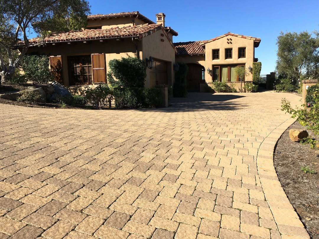 Desert-style stucco houses with a tan brick driveway and trees in bright sunlight