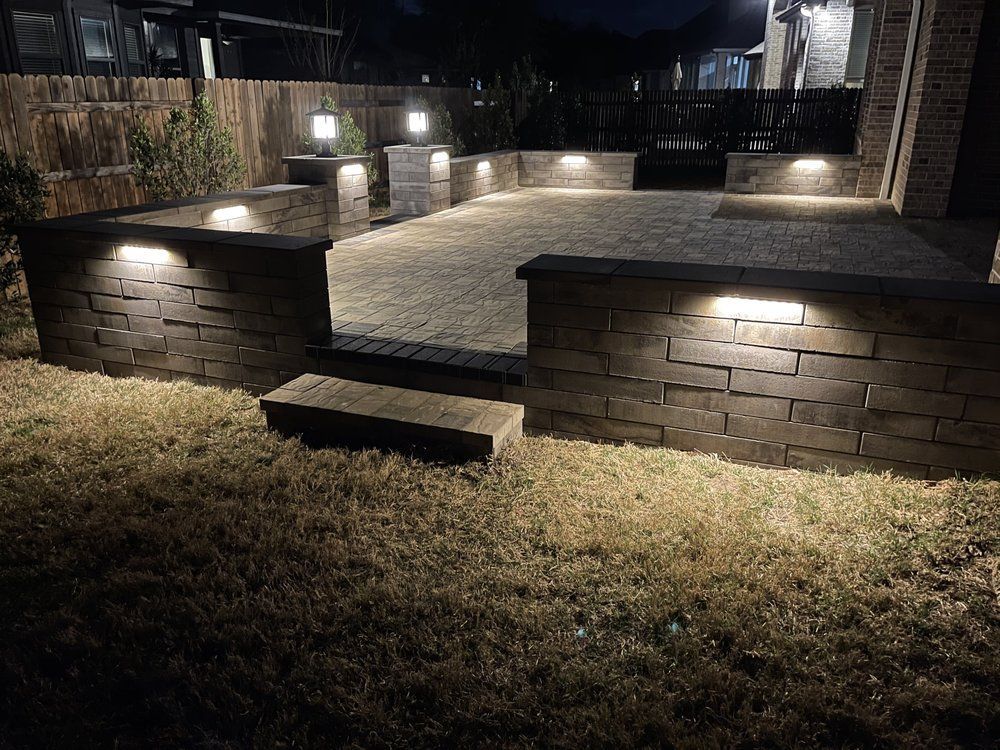 Backyard patio with stone walls, steps, and warm landscape lighting at night