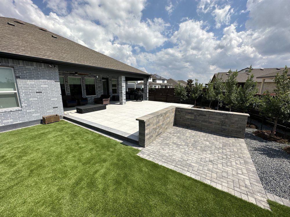 Modern backyard patio with stone retaining walls, pavers, and a green lawn beside a house