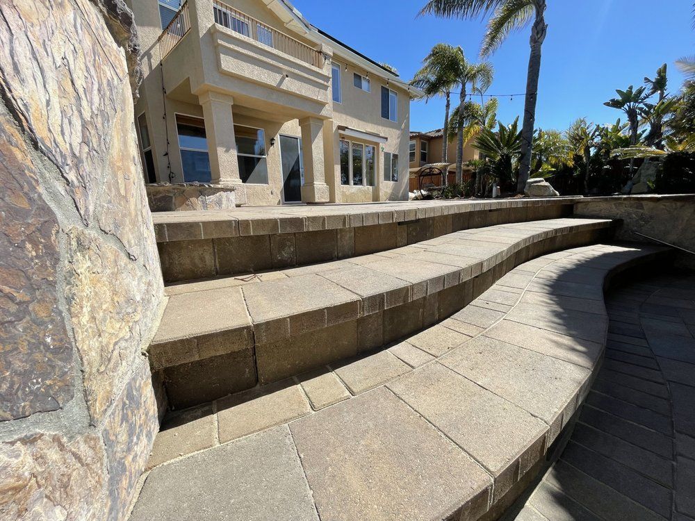 Curved stone steps and shaded walkway beside a luxury house with palm trees in bright sun