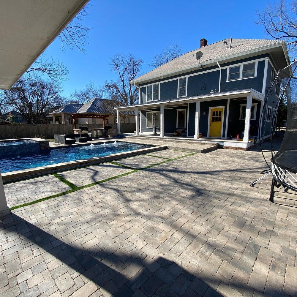 Backyard patio with pool beside a gray two-story house on a sunny day
