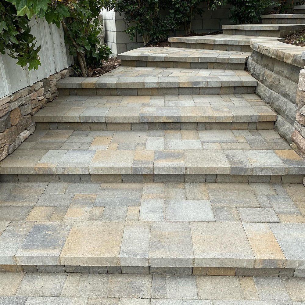 Stone steps with paver treads leading upward beside a stone retaining wall and greenery