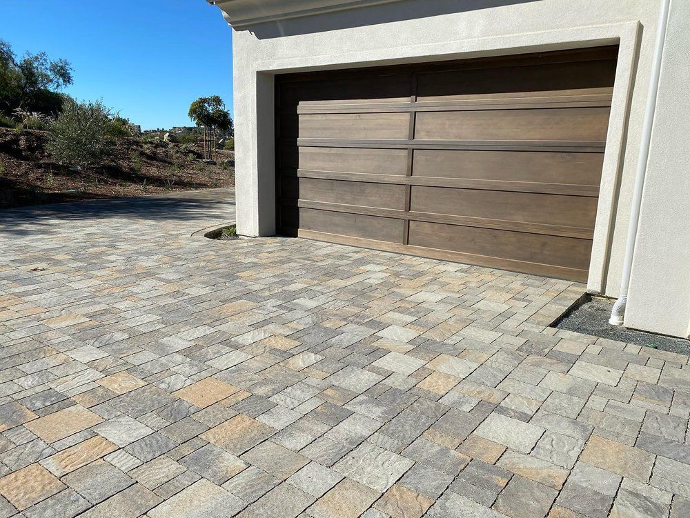 Modern home garage with a wooden door and stone-paved driveway in bright sunlight