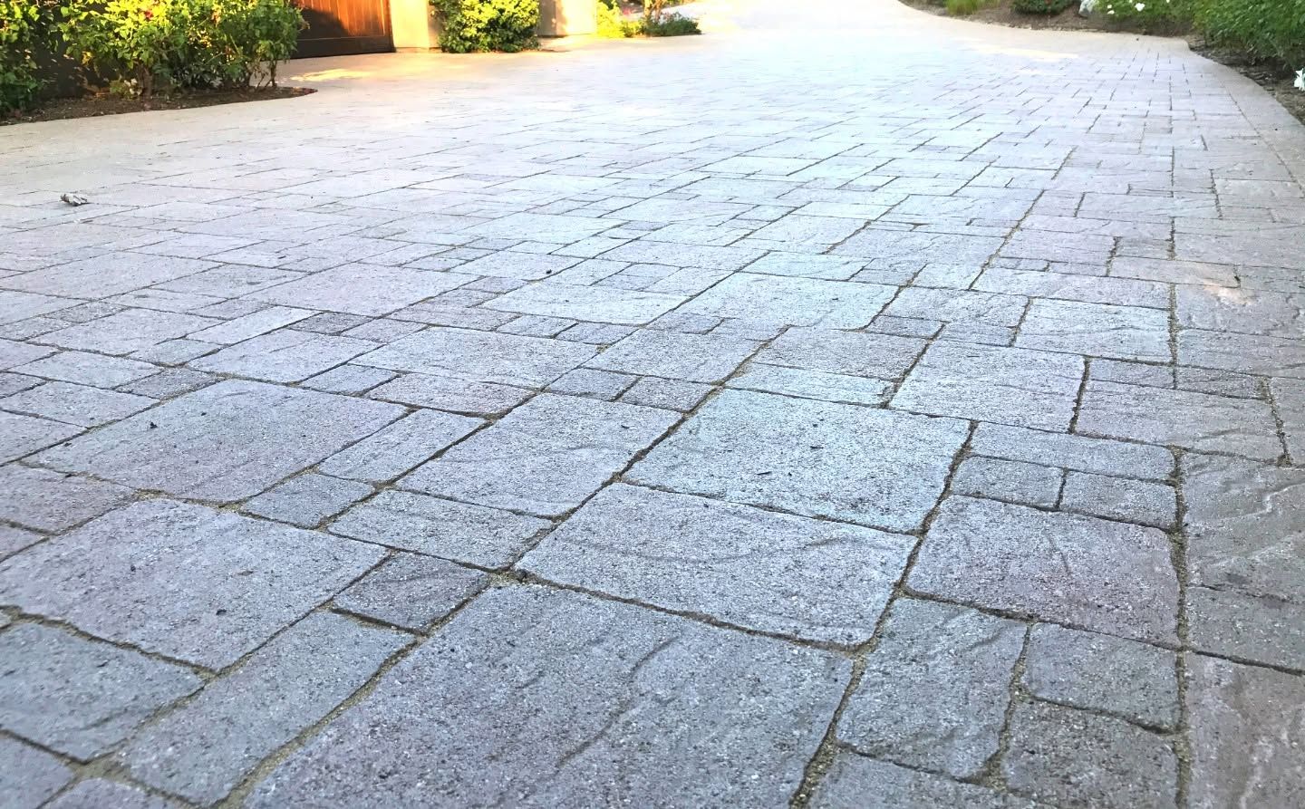 Empty stone-paved courtyard with bright sunlight and greenery at the edges