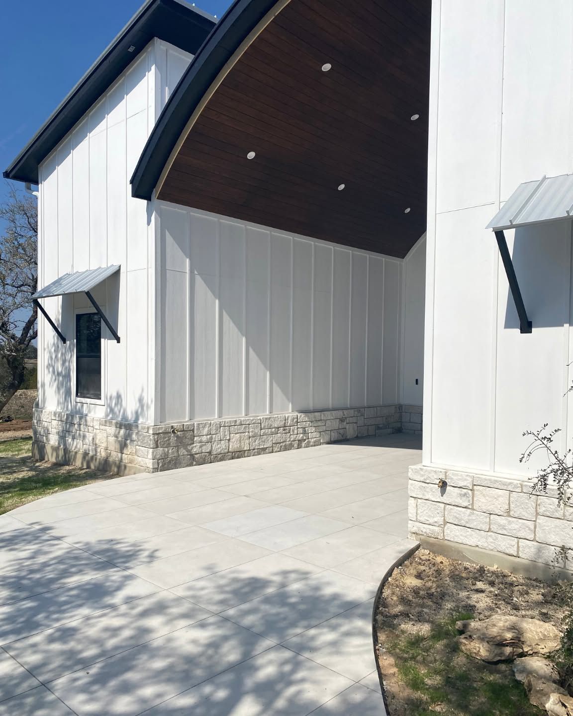 Modern white house exterior with stone base, covered entry, and curved concrete driveway.