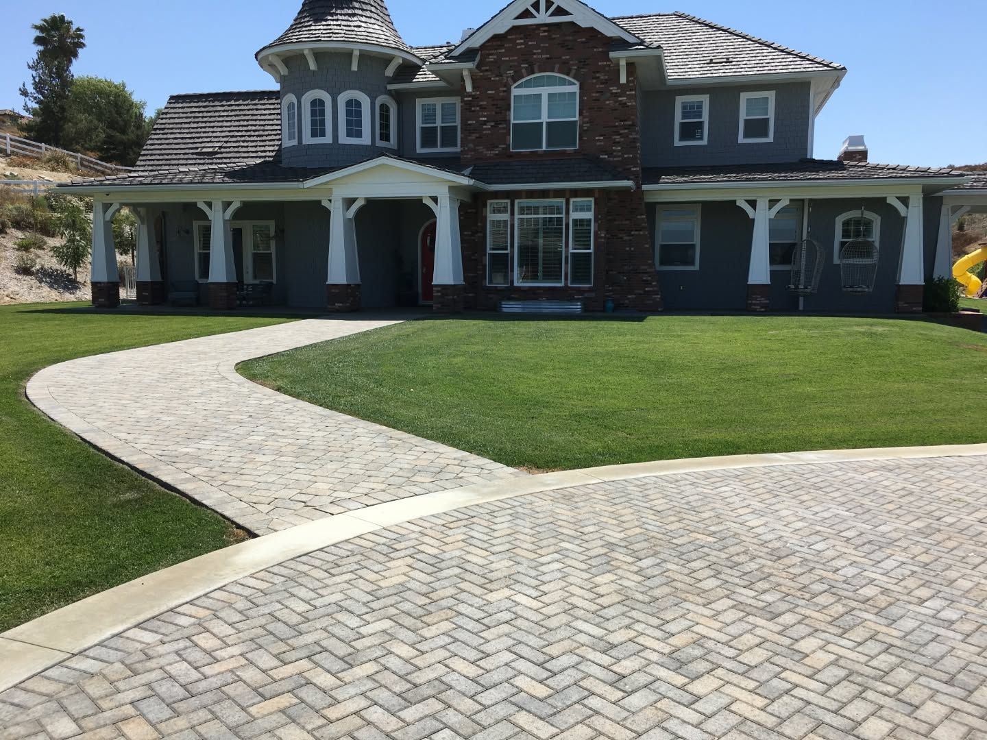 Large two-story gray house with a curved brick driveway and manicured green lawn