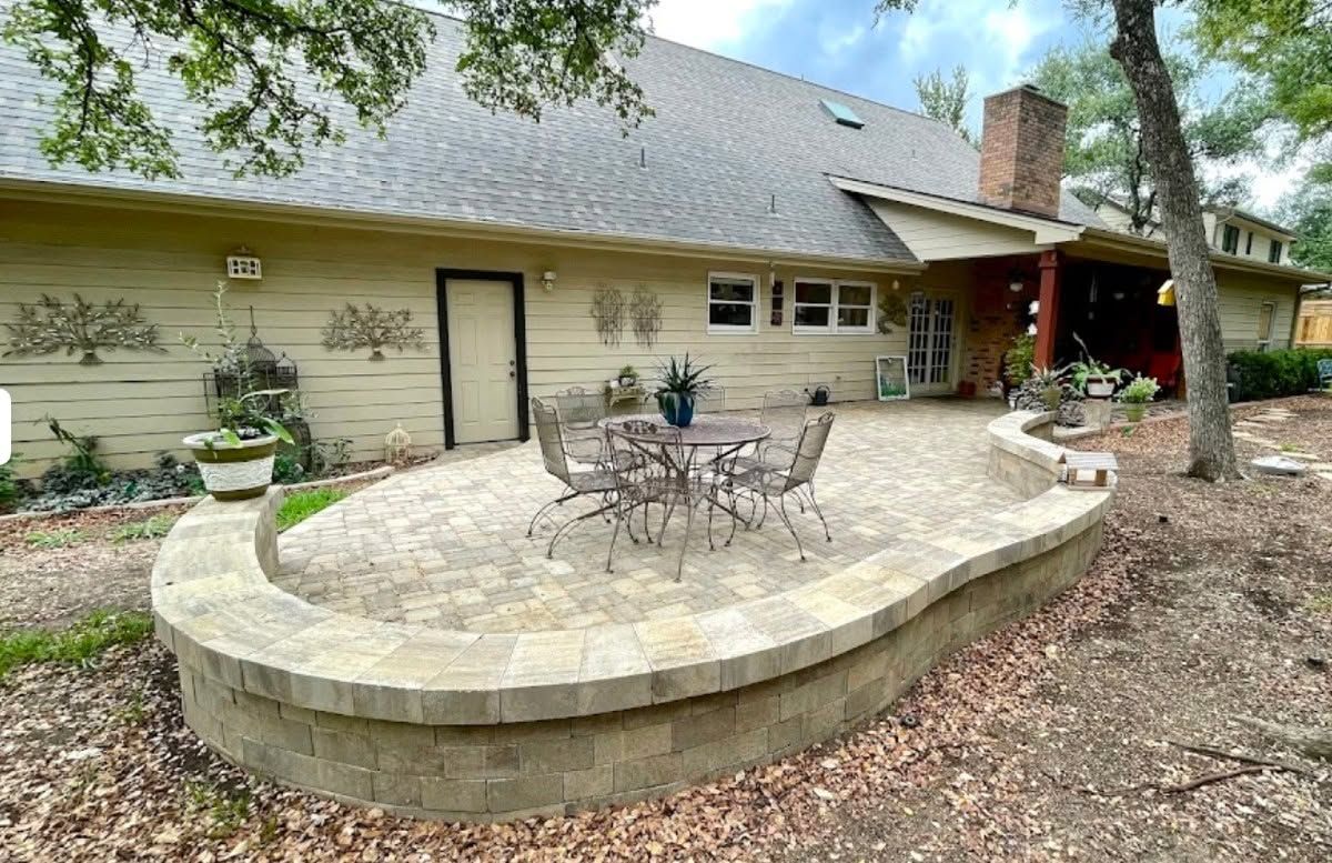 Stone patio with outdoor table and chairs beside a beige house and trees