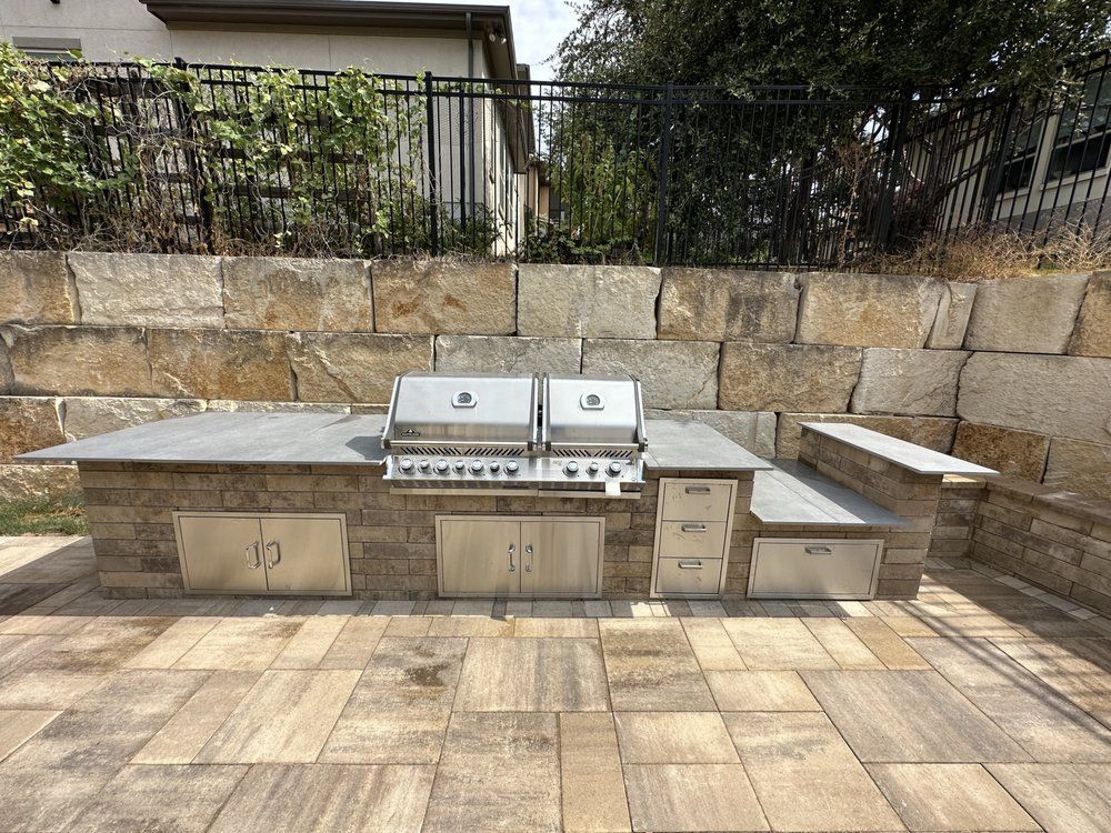 Outdoor stone patio with built-in stainless steel grill and countertop seating against a stone wall.