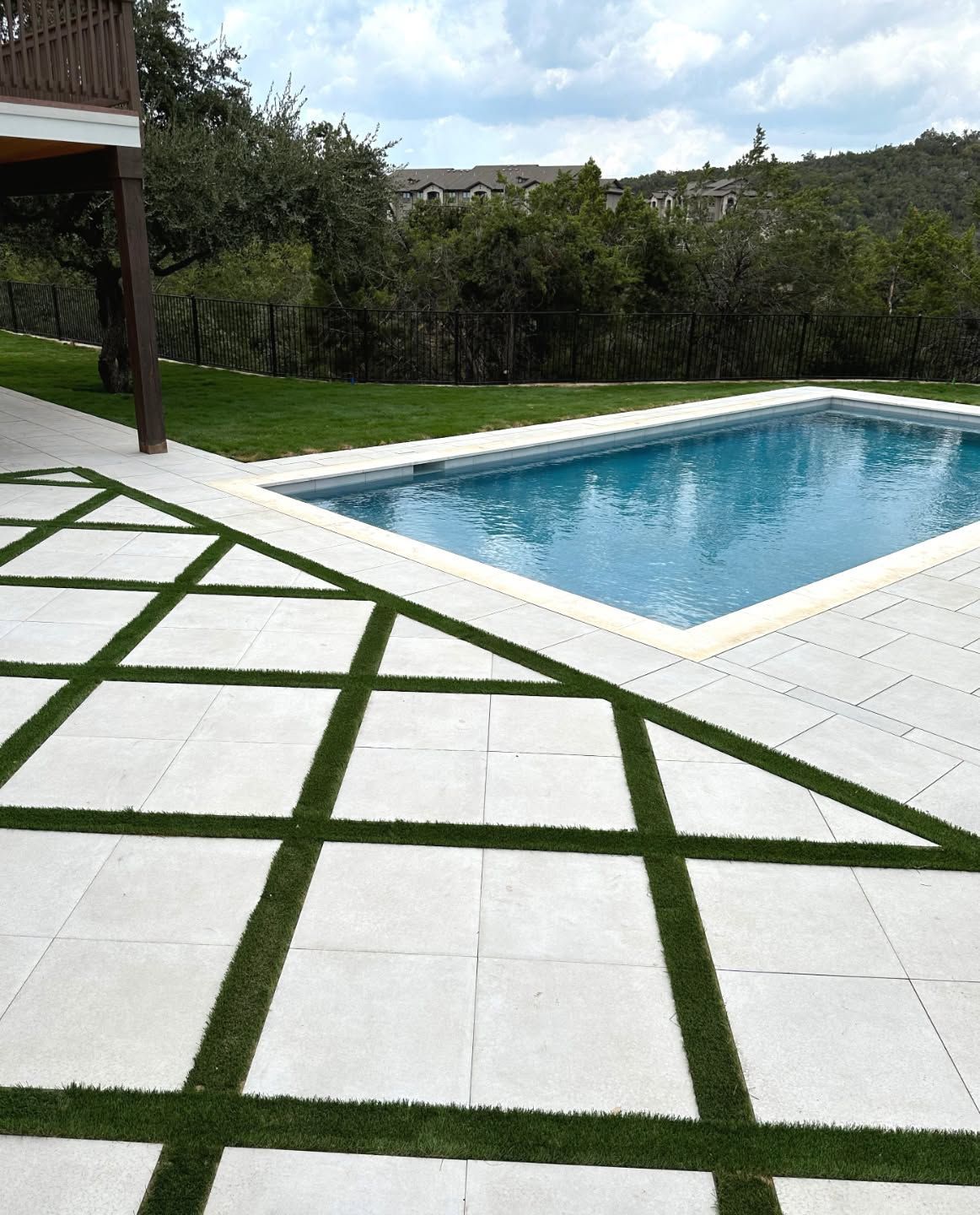 White-tiled patio with green grass grid leading to a blue swimming pool