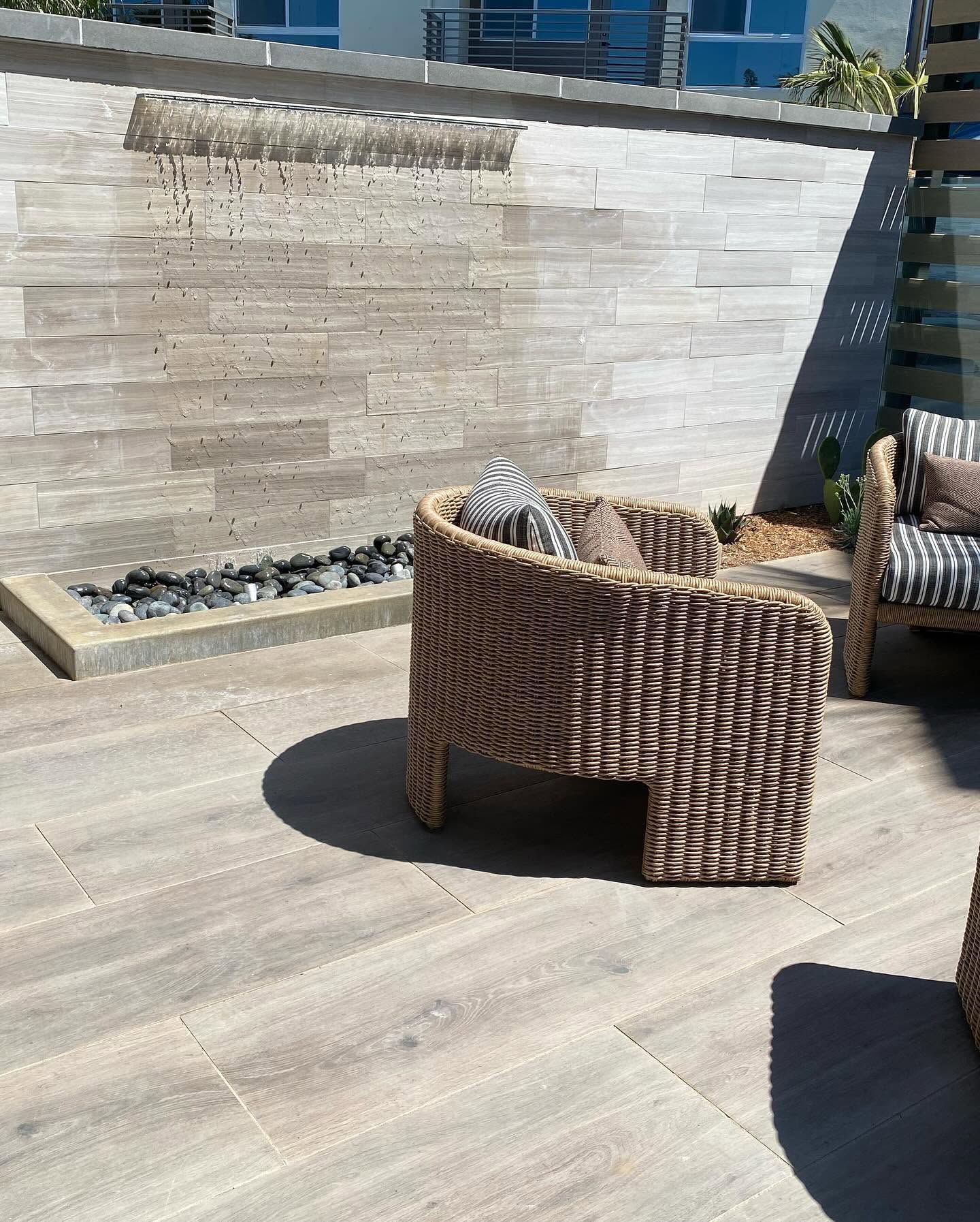 Outdoor patio with wicker chairs, stone wall fountain, and wooden deck in bright sunlight