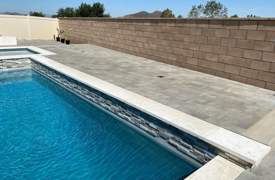 Swimming pool with concrete deck and brown privacy wall under a clear sky.