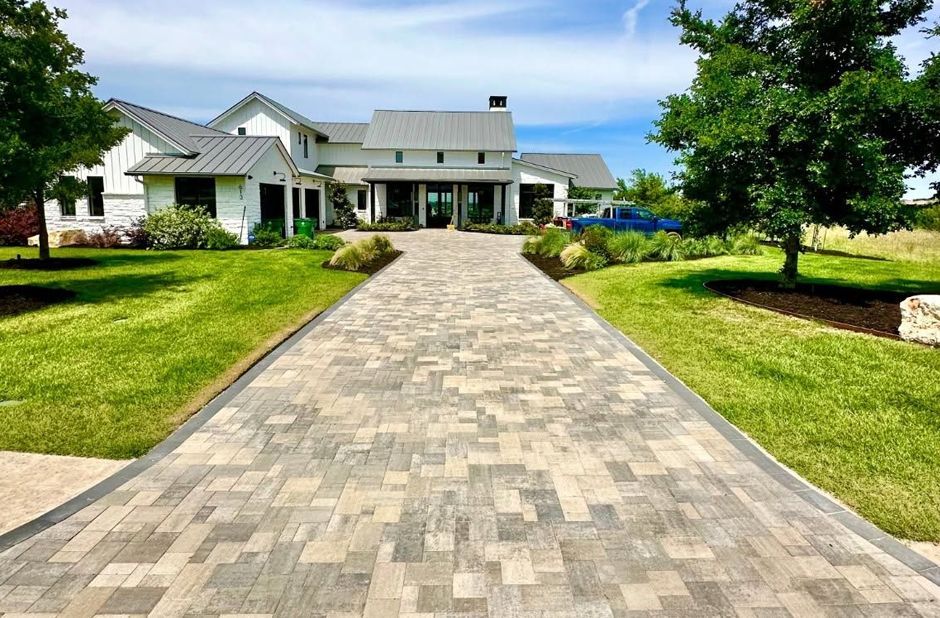 Stone walkway leading to a white house with a manicured lawn and trees under a blue sky.