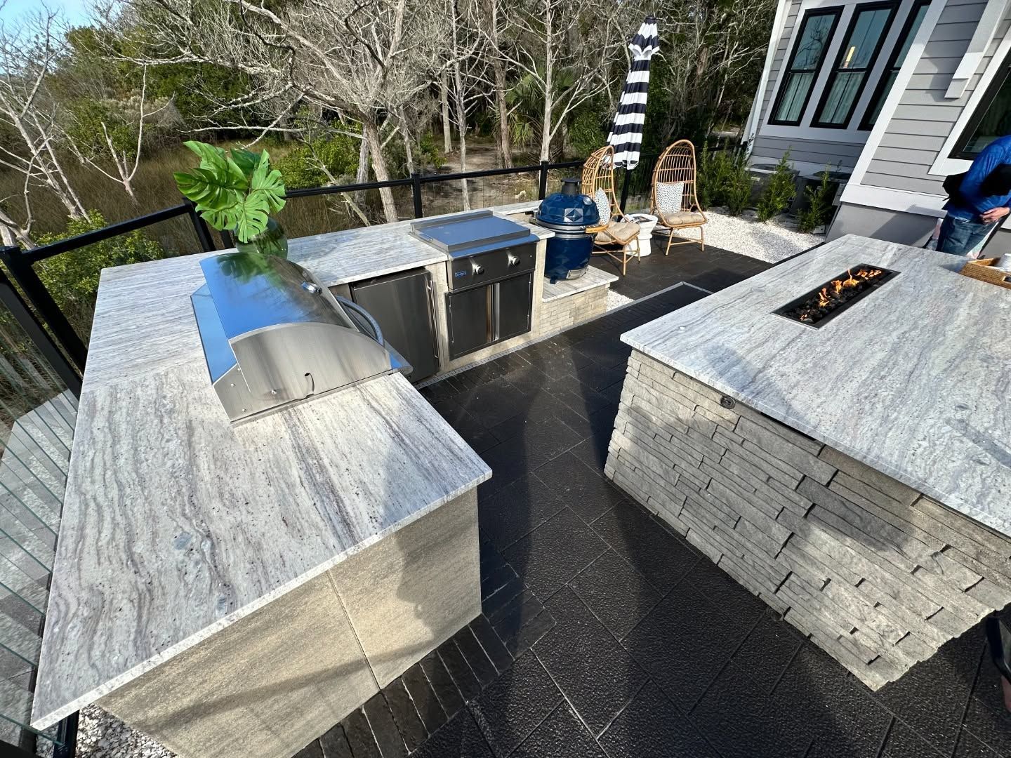 Outdoor patio with a stone kitchen island, grill, potted plants, and a black dining table by a house