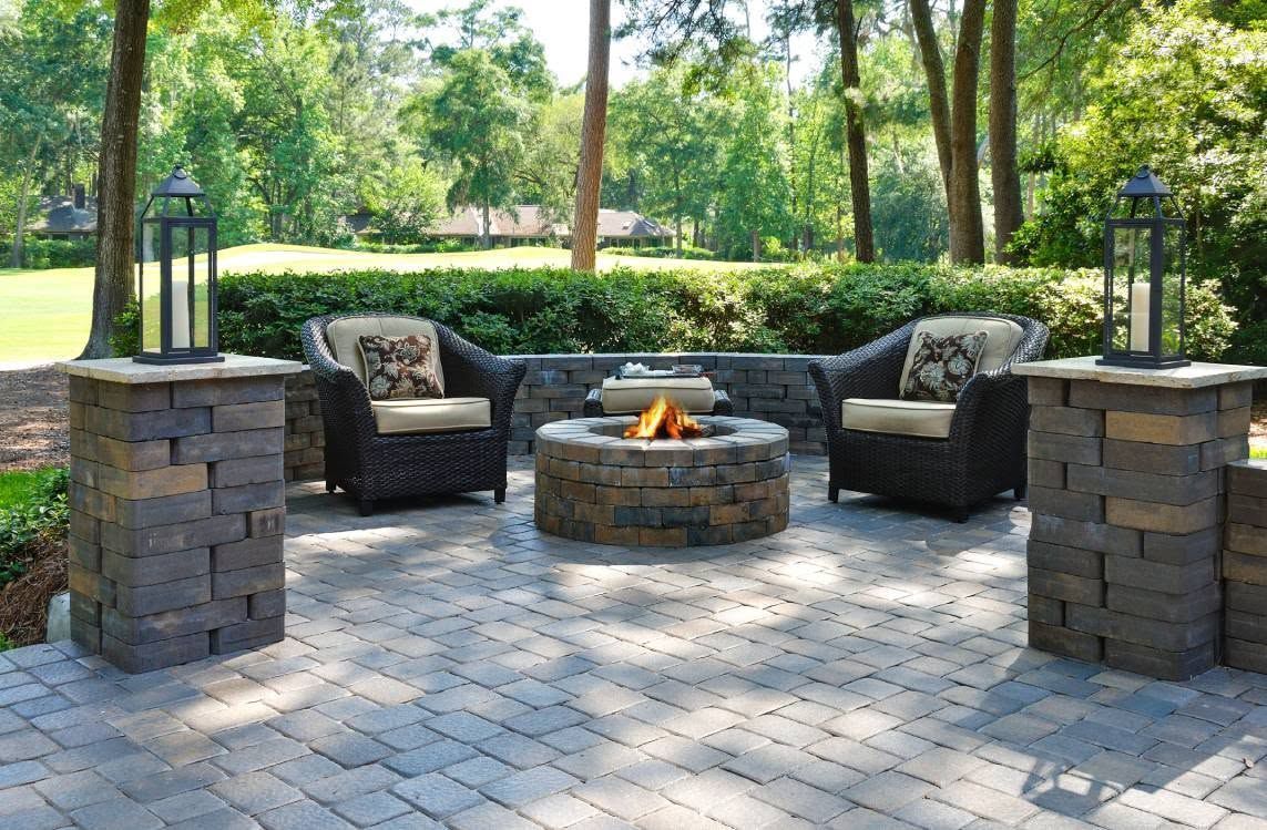 Stone patio seating area with wicker chairs around a fire pit in a landscaped backyard